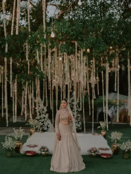 The bride posing in front of her wedding mandap, decorated with hanging floral arrangements.