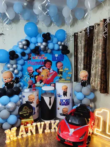A fun Boss Baby first birthday setup that includes a toy car for the birthday boy, along with character cutouts and a blue and silver balloon arrangement.