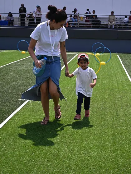 A mother and child walk hand-in-hand across the sports field, enjoying the day together.