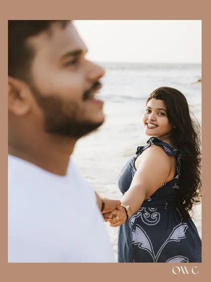 A playful "follow me to" style shot on the beach, capturing a candid moment of connection during a pre-wedding photoshoot.