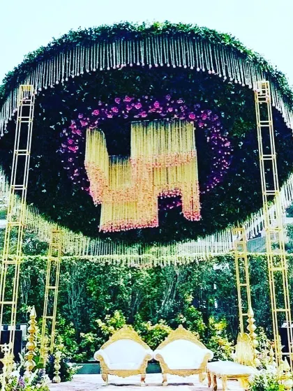 An extravagant outdoor wedding stage with a massive circular floral canopy. The hanging flower arrangement in the center adds a unique and luxurious touch to the decor.