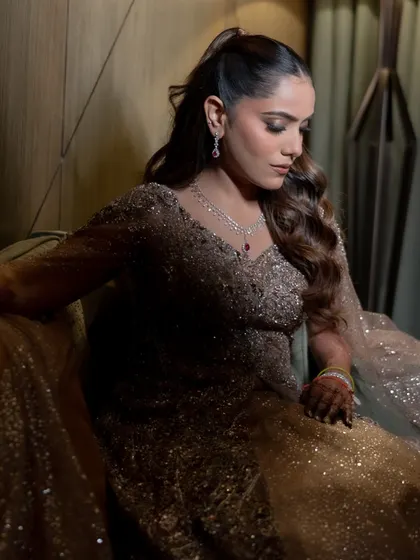 The bride looks radiant and happy, with her wavy ponytail adding a touch of playful elegance to her sparkling Sangeet gown.