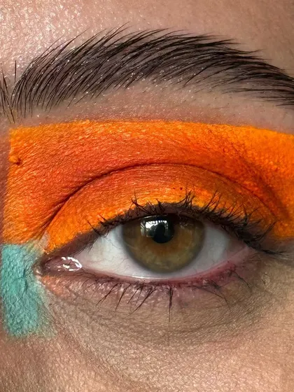 A creative, color-blocked eye makeup look. This graphic placement of bold orange and teal is a perfect example of using makeup as an art form.