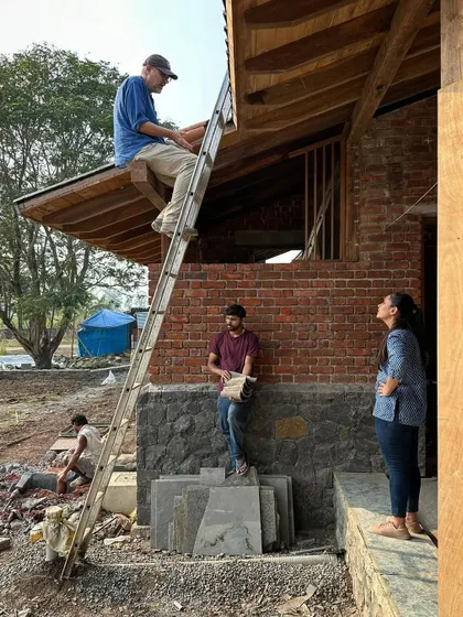 There is no substitute for being on-site to resolve complex details. Here, our principal architect is up on a ladder, working directly with the team to finalize the roofing details for the farmhouse.