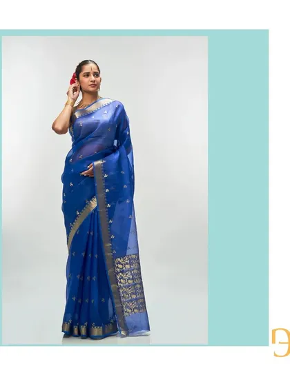 This cerulean blue silk organza saree features delicate gold zari buttis and a floral motif on the pallu, creating a rich, traditional look.
