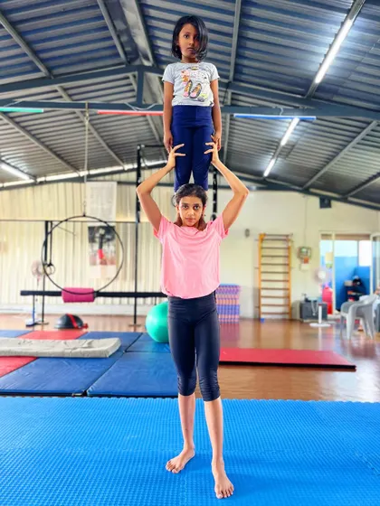 The concentration is real. This duo works on a shoulder stand, a foundational pose in partner acrobatics that builds strength for both the base and flyer.