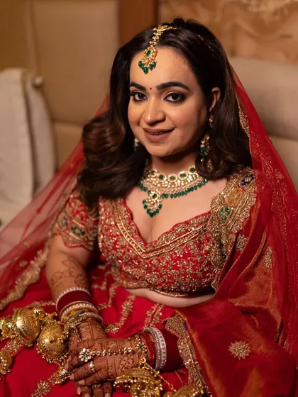 A close-up portrait of the bride, showcasing her beautiful makeup and the stunning emerald green jewelry we chose to contrast with her red lehenga.