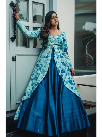 A fashion-forward pose in a blue and green floral fusion lehenga. The model holds the door handle, adding a dynamic line to the composition and showcasing the outfit's design.