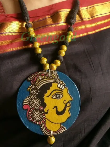 Another example of a Kalamkari fabric pendant, this time featuring the face of a royal figure with a magnificent mustache. The yellow and blue colors are characteristic of this art form.