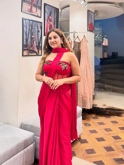A side view of the red corset saree, showing how the drape falls beautifully. The sheer panel on the corset adds a modern touch, making it a sophisticated choice for a cocktail party or reception.