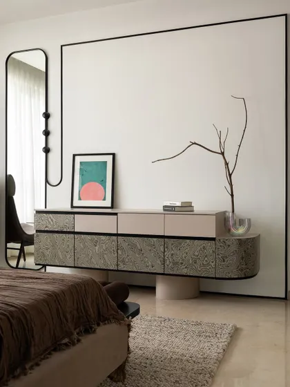 The floating console and full-height mirror create a sense of lightness in the bedroom. The blank wall space is intentional, allowing the custom furniture and curated art to become the focus, embodying our 'less is more' approach.