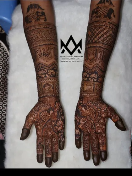 Traditional bridal mehendi featuring classic motifs like peacocks, bride and groom figures (dulha-dulhan), and elephants, covering the arms from palm to elbow.