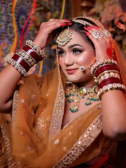 A graceful pose where the bride adjusts her maang tikka. This shot highlights her elegant hand gestures and the intricate details of her head jewellery.