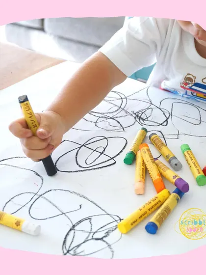 Every mark a child makes is meaningful. Here, a toddler explores mark-making with crayons, a fundamental step in developing the fine motor skills and hand-eye coordination needed for writing and drawing later on.