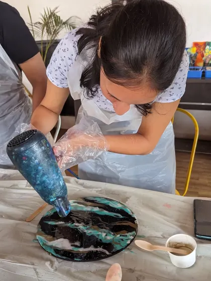 Using a heat gun is a key step in resin art to remove bubbles and create beautiful cell effects in the pigments, as demonstrated by this participant working on her beach clock.