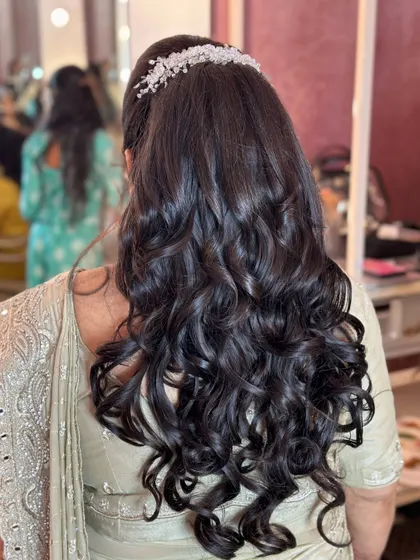 A voluminous ponytail with soft curls, finished with a sparkling hair accessory for a chic party look for a wedding guest.