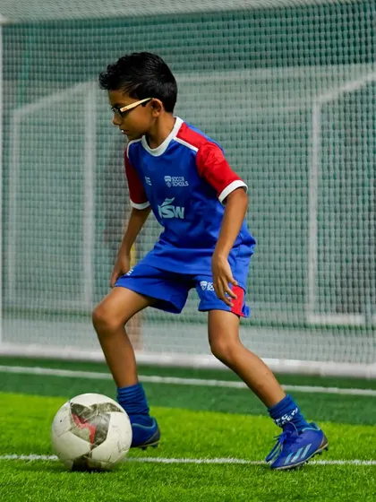 A young player with glasses shows that football is for everyone. He focuses intently on controlling the ball during a drill.
