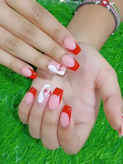 A modern French manicure in red, with a playful heart-shaped cutout and abstract swirl designs.