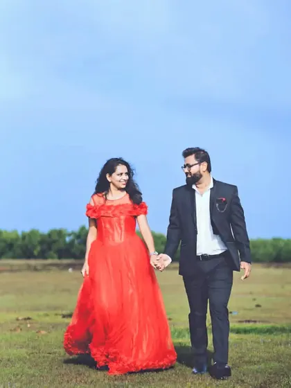 A romantic walk through a field. The bride-to-be is wearing a beautiful red gown with rose-like details on the skirt, a perfect choice for a nature-filled photoshoot.