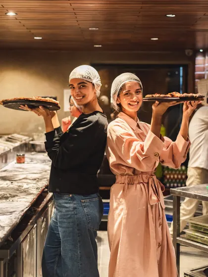 Two happy customers posing with the pizzas they made themselves at our workshop.