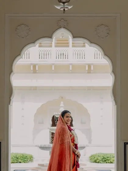 A portrait of the bride, Nikita, framed by the beautiful arches of her Jaipur wedding venue, looking regal and serene.