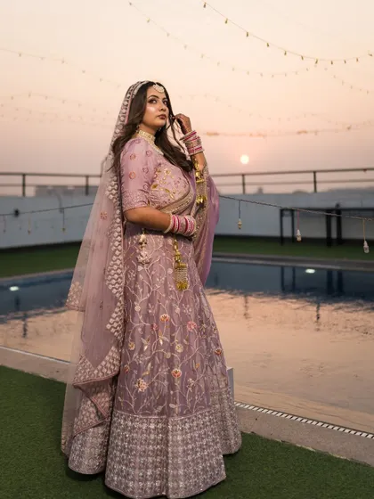 A full-length portrait of the bride, Nitika, showcasing her stunning lilac lehenga against the sunset sky.