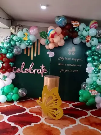 A vibrant and colorful "Celebrate" backdrop. I used a dark green backdrop and created an organic balloon arch with a mix of green, red, and pastel balloons, accented with butterfly and baby-themed props.