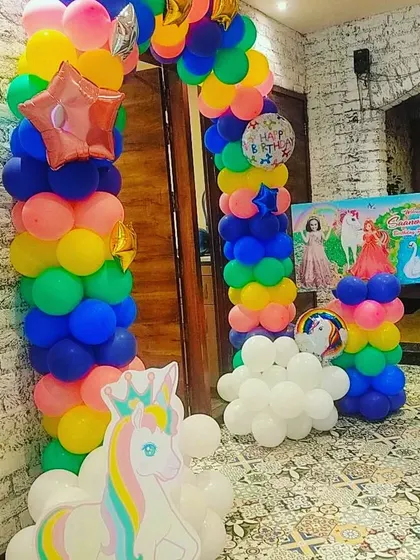 A rainbow and unicorn themed party entrance, with a colorful balloon arch and a unicorn cutout to welcome guests.