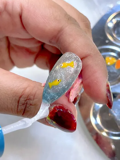A behind-the-scenes shot from a look-and-learn seminar, showing the creation of an aquarium nail with tiny fish.