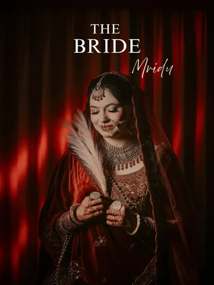 A creative bridal portrait with a feather prop. The bride, in her deep red velvet lehenga, looks serene and divine, creating a unique and artistic image that feels like a painting.