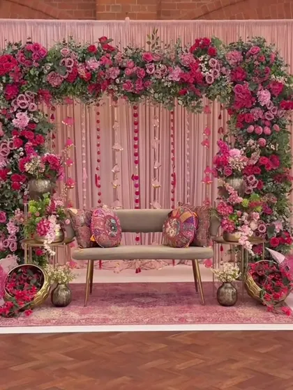 We design elegant and romantic themes for Mehendi ceremonies, like this lush pink floral arch. The setup includes coordinated seating, printed cushions, and traditional decorative umbrellas to complete the look.