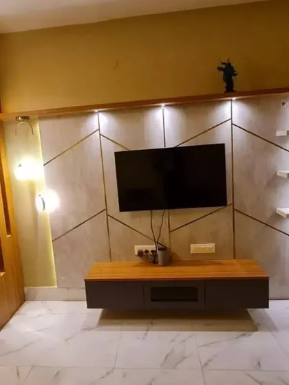This living room in Kolkata features a striking TV wall with geometric patterns, floating shelves, and integrated lighting for a contemporary look.