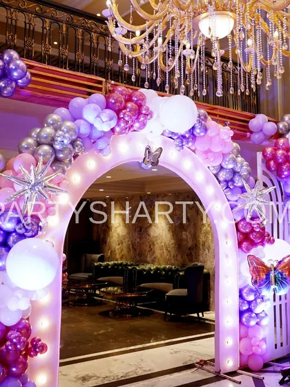 A grand lighted archway decorated with purple and silver balloons and starburst accents, creating a magical entrance for a princess and butterfly-themed event.
