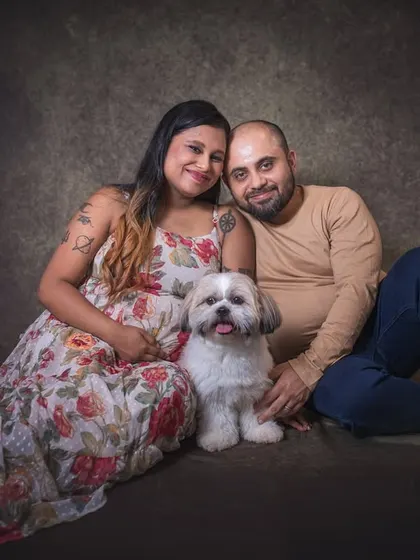 A relaxed and happy portrait of an expecting couple sitting on the floor with their dog nestled between them. This image radiates warmth and the love they share for their pet and each other.