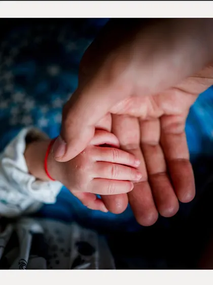 A close-up of a baby's tiny hand resting in their parent's palm, a simple yet profound image from a naming ceremony.