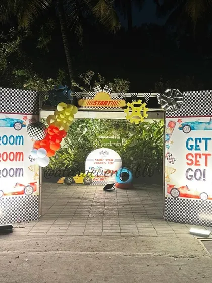 The entrance to a race car-themed second birthday party at night. The checkered flag-style gates and "Vroom Vroom" signs create an exciting and dynamic entry for the celebration.