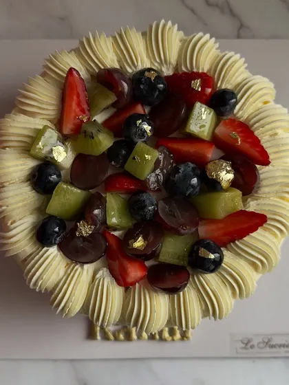 A top-down view of the Fresh Fruit Cake, showcasing the vibrant colors and generous topping of mixed fruits with a touch of gold leaf.