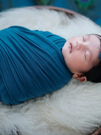 A variation of our peacock theme, with the baby wrapped snugly and adorned with a matching blue headpiece featuring a peacock feather.