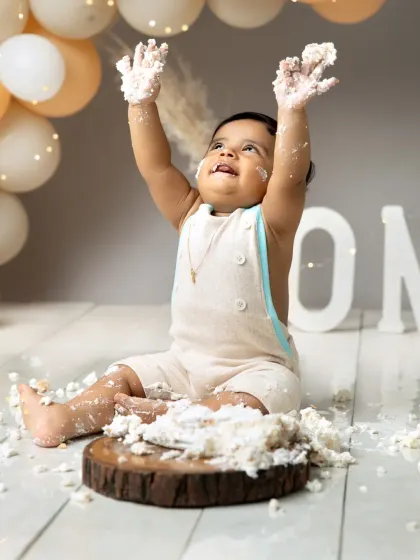 Hands up if you love cake. This little boy is celebrating his first birthday with a joyful throw of frosting, set against a modern backdrop of neutral-toned balloons.