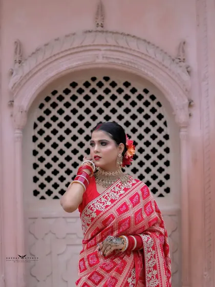 A three-quarter shot with the woman posing against a latticed window (jaali). The architectural detail adds texture and interest to the background.