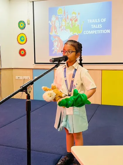 Using hand puppets, a student confidently narrates a story on stage, demonstrating her public speaking and creative talents.