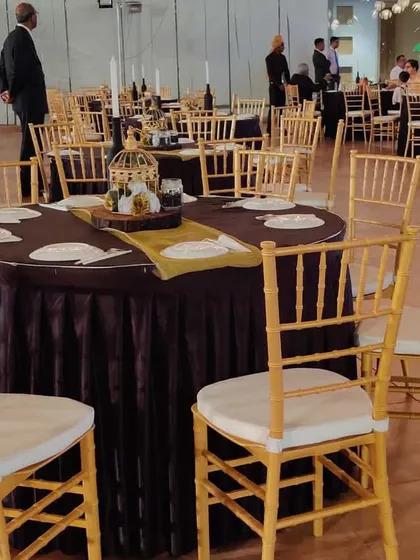 A closer look at a table setting for a formal corporate dinner. The use of dark, rich tablecloths with elegant gold Chiavari chairs and simple centerpieces creates a classic and professional look suitable for any high-profile company function.