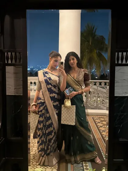 A mirror selfie moment with a friend. It shows how two different saree styles, one in cool navy and one in deep green, can complement each other perfectly.