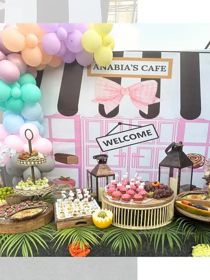 A whimsical setup for a child's birthday party, "Anabia's Cafe". The table is filled with kid-friendly treats like cupcakes and fruit platters, presented with a fun, colourful cafe theme.