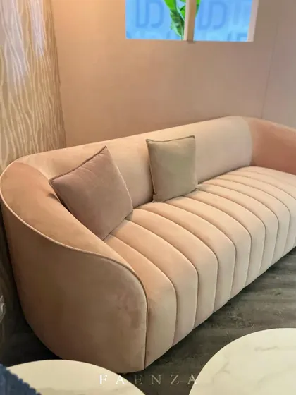 A beautifully crafted sofa with vertical channel tufting in a soft blush pink velvet. The curved silhouette and elegant design make it a standout piece, perfect for adding a touch of gentle color and sophistication.