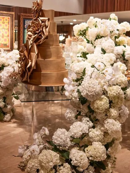 A magnificent golden cake surrounded by a cascade of white hydrangeas and orchids. This dessert display is a work of art, serving as a stunning focal point for the celebration.