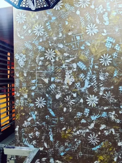 This close up highlights the details of an abstract, multi layered stencil effect. The combination of metallic gold, white, and blue creates a dynamic and modern piece of wall art.