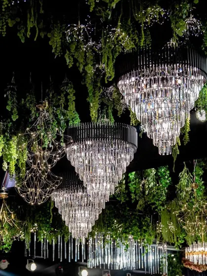 A breathtaking ceiling installation for a grand reception. Massive crystal chandeliers hang amidst lush green foliage, creating a feeling of being in an enchanted forest.