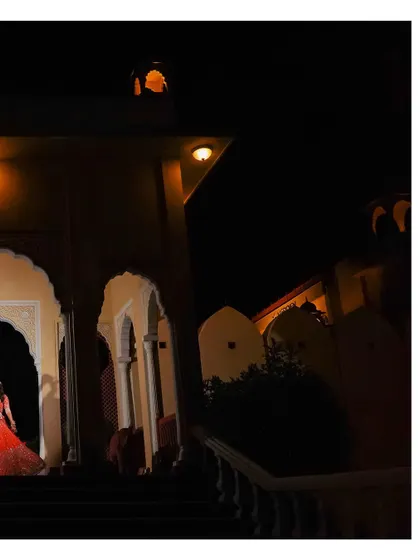A wide, atmospheric shot of the bride at night. The dramatic lighting of the venue creates a cinematic and mysterious feel for this unique bridal portrait.