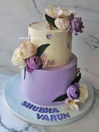 An engagement cake in lilac and off-white. This two-tier chocolate mousse cake has a modern, artistic feel with its fault line design and floral decorations.